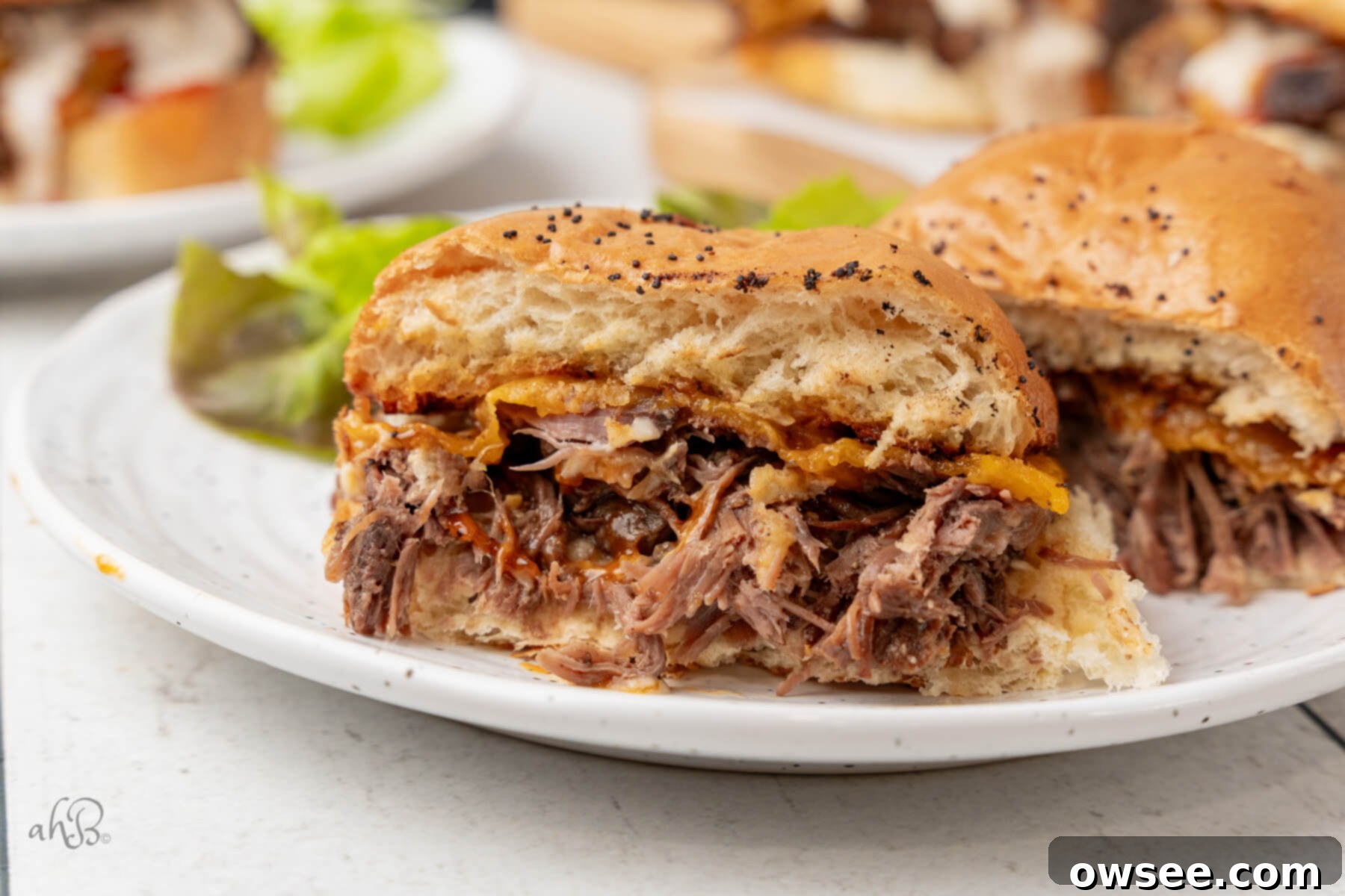 A homemade Crockpot Beef 'N Cheddar sandwich, cut in half to reveal layers of tender shredded beef and gooey melted cheddar, presented on a pristine white plate.