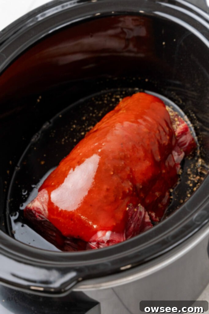 The chuck roast, beef consommé, and seasonings are carefully added to the crockpot for slow cooking.