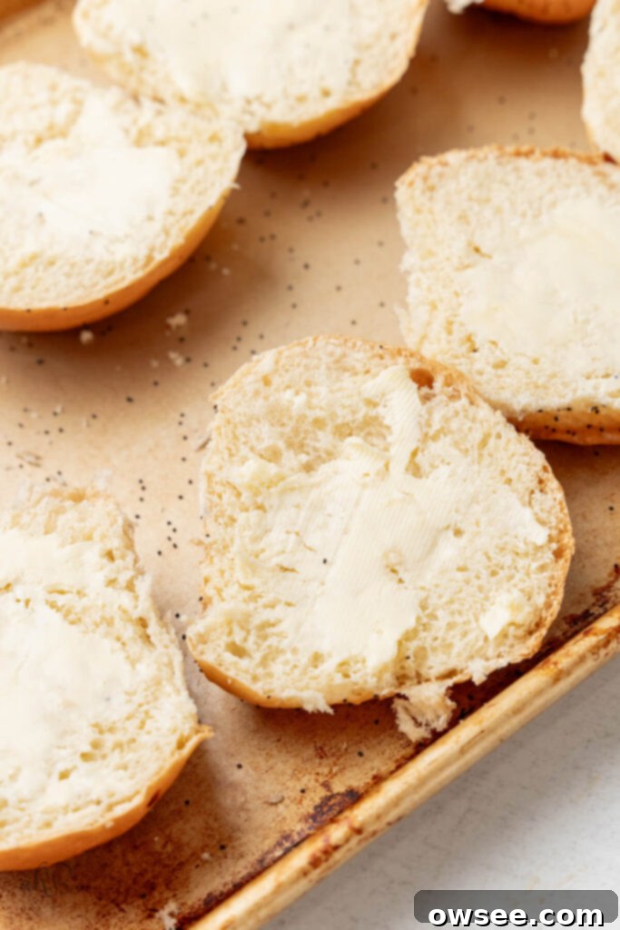 The onion buns, freshly buttered on their cut surfaces, are perfectly arranged on a baking sheet, ready for a quick toast under the broiler.