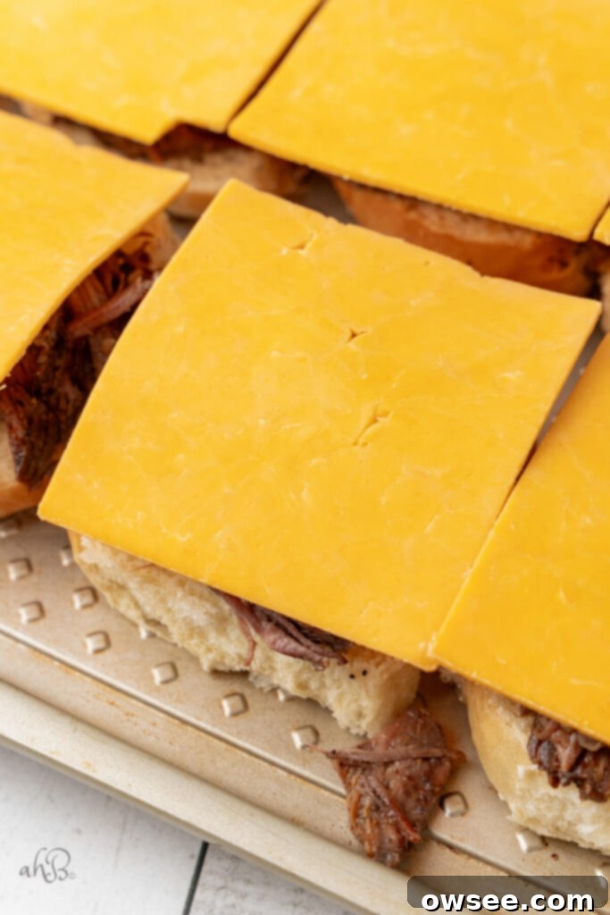 The shredded beef and cheddar cheese are carefully placed on the bottom halves of the toasted buns, waiting for the broiler to work its magic.