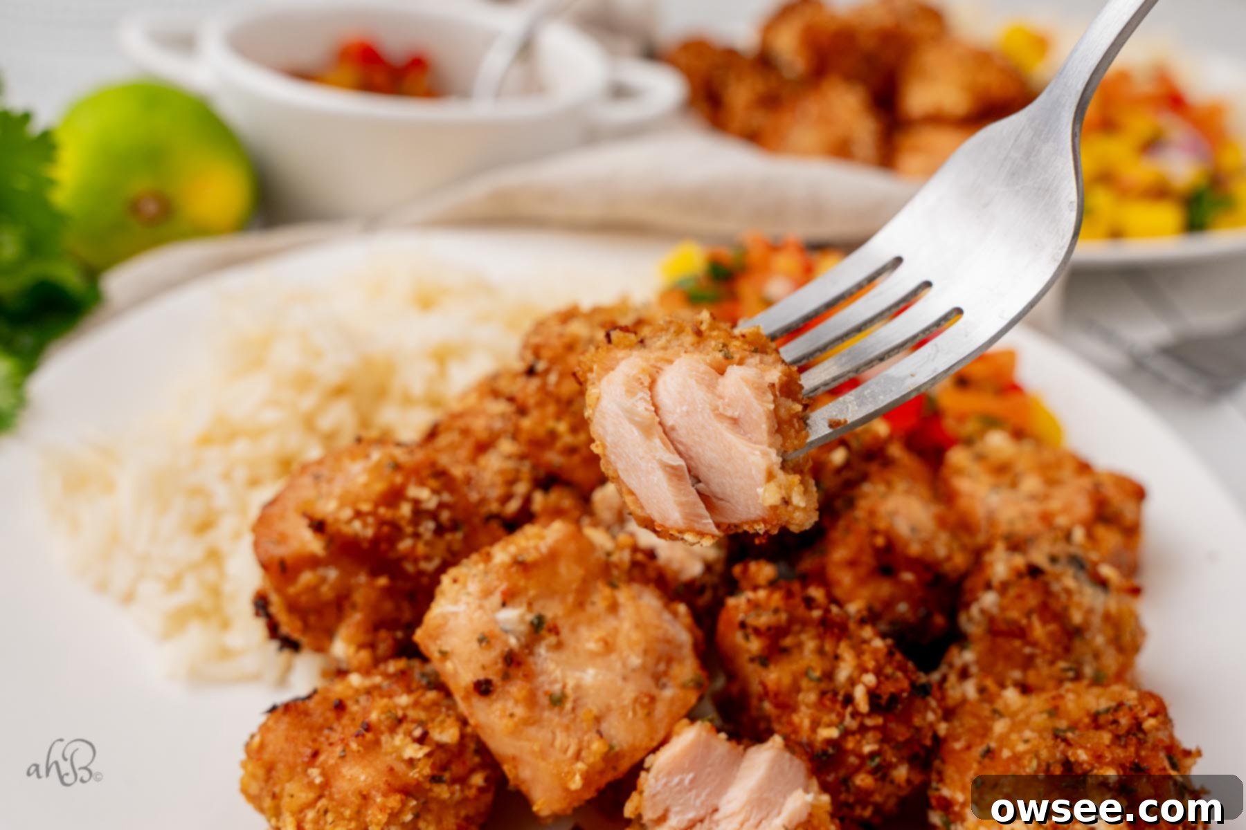 Air Fryer Hot Honey Salmon Bites 2 Half of a salmon bite is held on a fork over a plate of salmon bites and rice, showcasing its crispy exterior and tender inside.