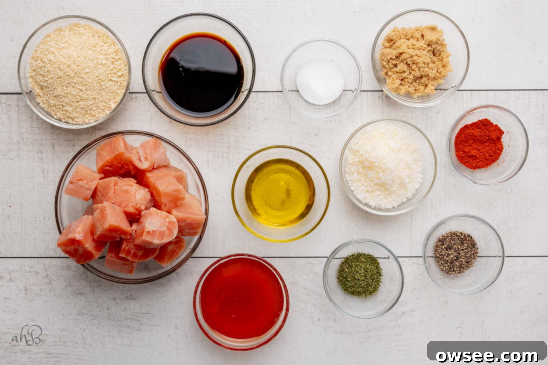 Air Fryer Hot Honey Salmon Bites 4 The ingredients for salmon bites are separated into clear glass bowls, including salmon, sauces, breadcrumbs, cheese, and spices.