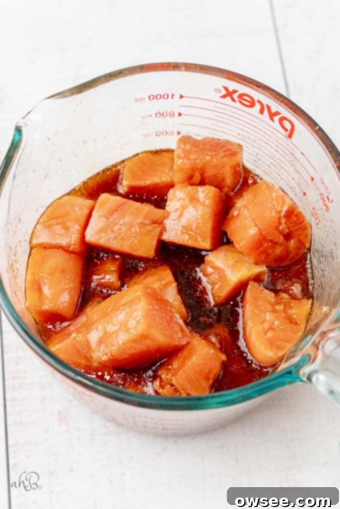 Air Fryer Hot Honey Salmon Bites 5 Cubed salmon bites are shown marinating in a flavorful mixture within a clear measuring bowl.