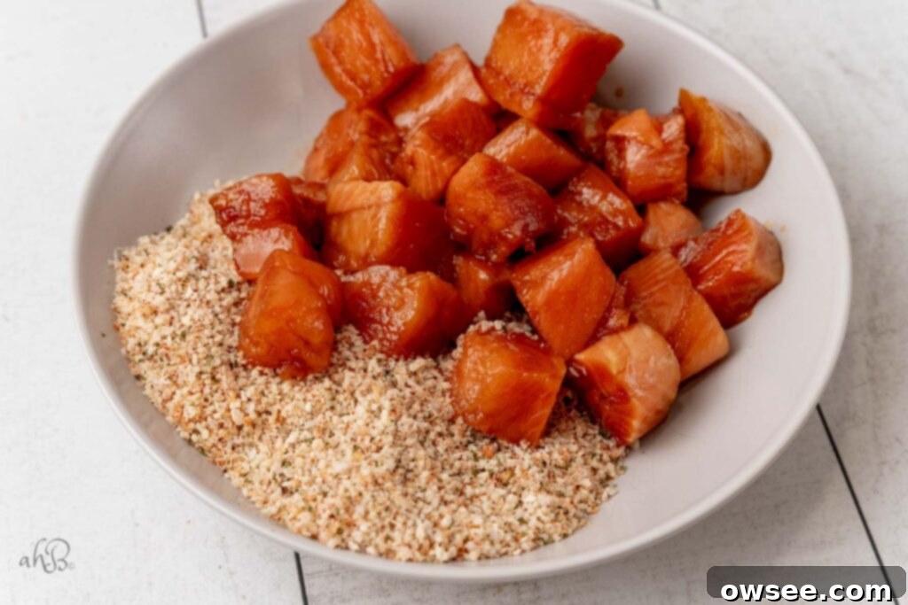 Air Fryer Hot Honey Salmon Bites 7 Marinated salmon bites are being tossed with the breadcrumb mixture in a bowl, ensuring even coating.
