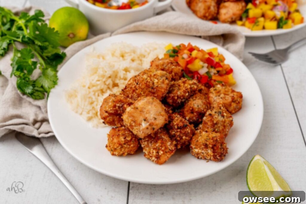 Air Fryer Hot Honey Salmon Bites 9 A white plate is full of perfectly cooked, golden-brown air fryer salmon bites, garnished with fresh cilantro, ready to be served.