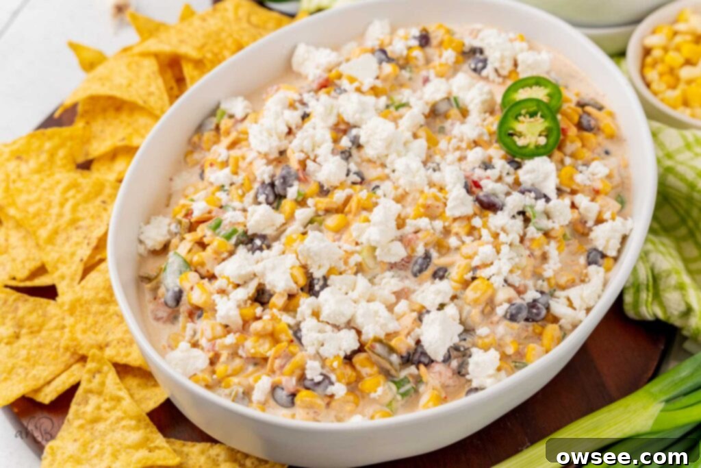 A white serving bowl brimming with colorful Fiesta corn dip, accompanied by a pile of crispy tortilla chips on the side, ready for dipping.