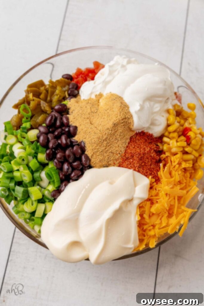 Step 1: All the colorful ingredients for Fiesta Corn Dip, including corn, beans, cheese, and dressings, are placed together in a large mixing bowl, ready to be combined.