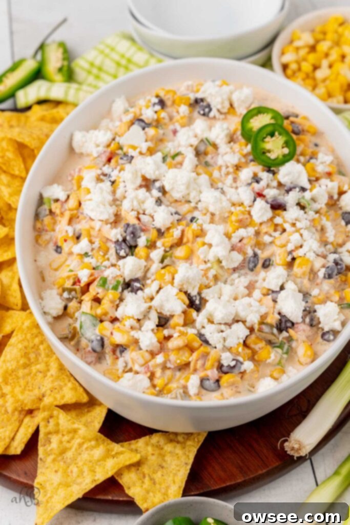 Step 3: A close-up of Fiesta Corn Dip in a white serving bowl, topped with crumbled queso fresca cheese and garnished with fresh sliced green onions, ready to be served.
