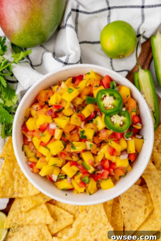 Tropical Heat Mango Salsa 2 A white bowl of spicy mango salsa with a pile of tortilla chips to one side and limes to the other.