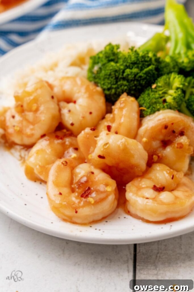 Honey Garlic Glazed Shrimp 2 A white plate with a serving of sticky honey garlic shrimp and steamed broccoli to one side.