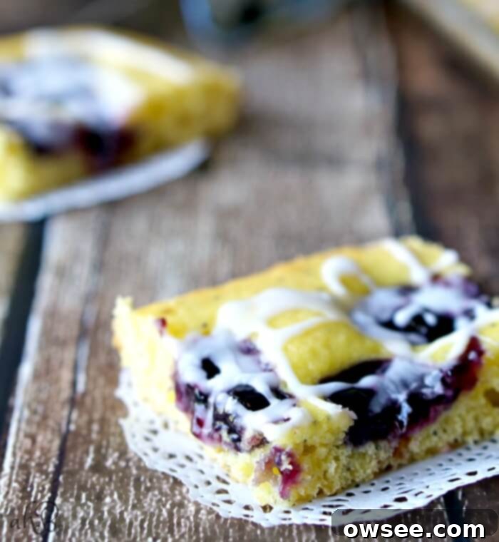 A freshly baked pan of Lemon Poppy Seed Blueberry Squares with lemon glaze, sliced and ready to serve.