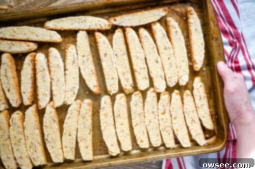 Chocolate almond biscotti slices neatly arranged on a baking sheet, cut side down, for their second bake.