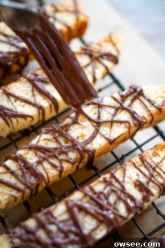 Finishing Chocolate Almond Biscotti by drizzling melted chocolate over the cooled cookies with a fork.