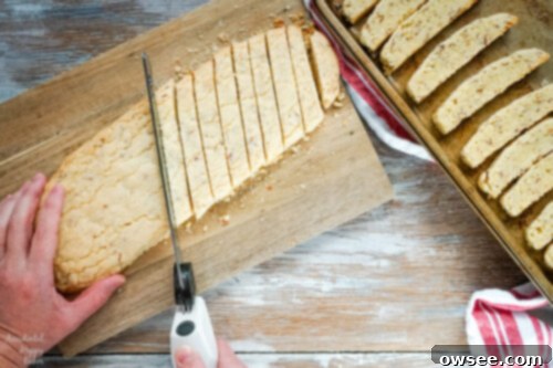 Slicing a baked chocolate almond biscotti loaf diagonally into uniform 1/2 inch pieces using a serrated knife.