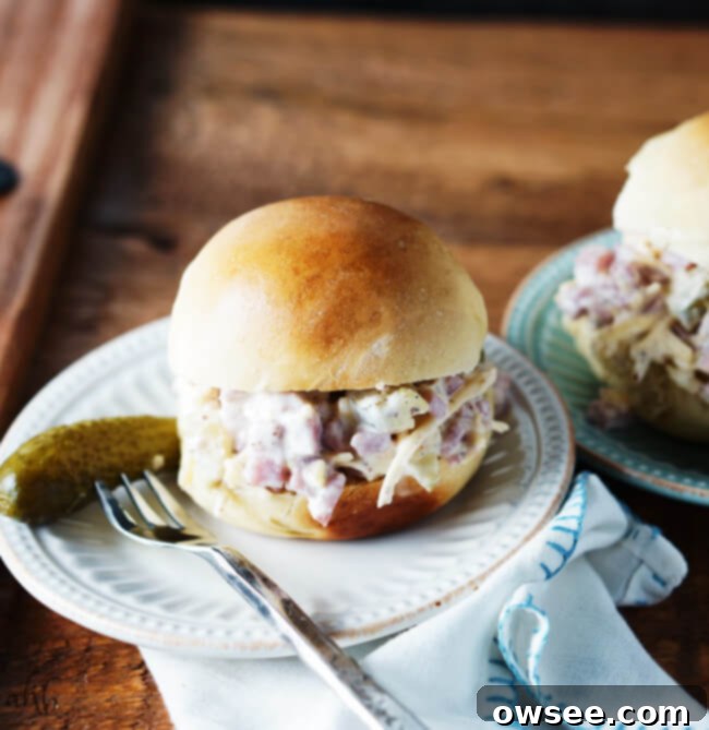 A slider bun filled with cuban ham salad on a plate with a dill pickle next to it. 