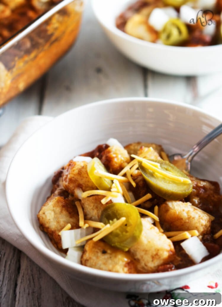 A white bowl with a serving of Chili Cheese Tater Tot Casserole, topped with chopped onions and jalapenos. 