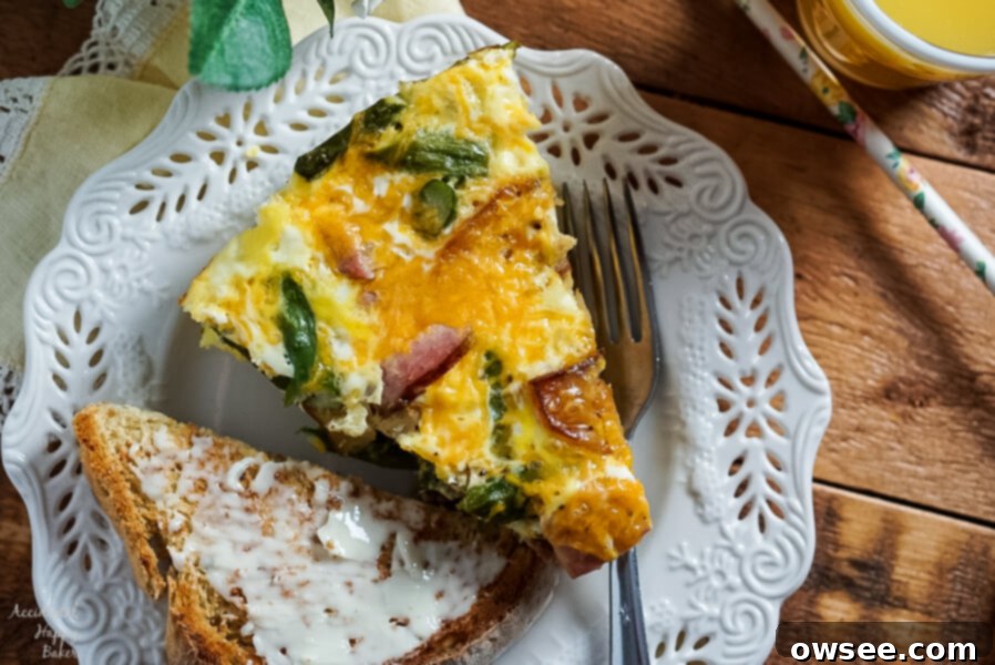 A slice of Ham, Asparagus, and Potato Frittata on a plate next to buttered toast and juice for a complete meal. 