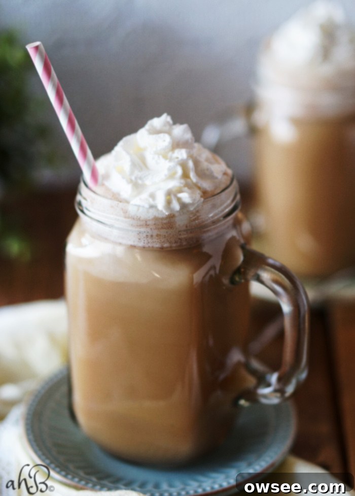 Two mugs of Hot Buttered Kahlua, garnished with a cinnamon stick, on a rustic wooden surface.