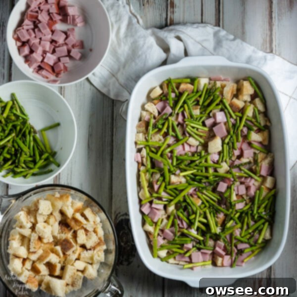 Layering the delicious ham, asparagus, and cheese over English muffins in a baking dish for the make-ahead strata.