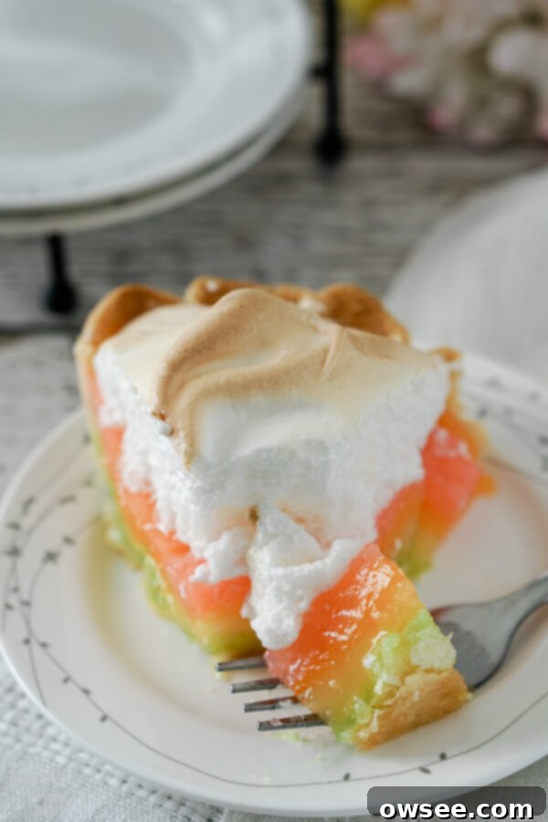 A fork lifts a bite of rainbow lemon meringue pie, showing the distinct colored layers of filling.