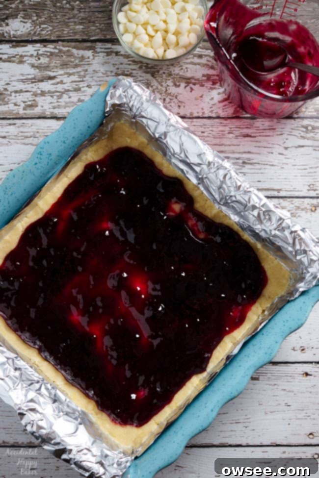 Next, a layer of vibrant raspberry jam is spread evenly over the pressed shortbread dough.