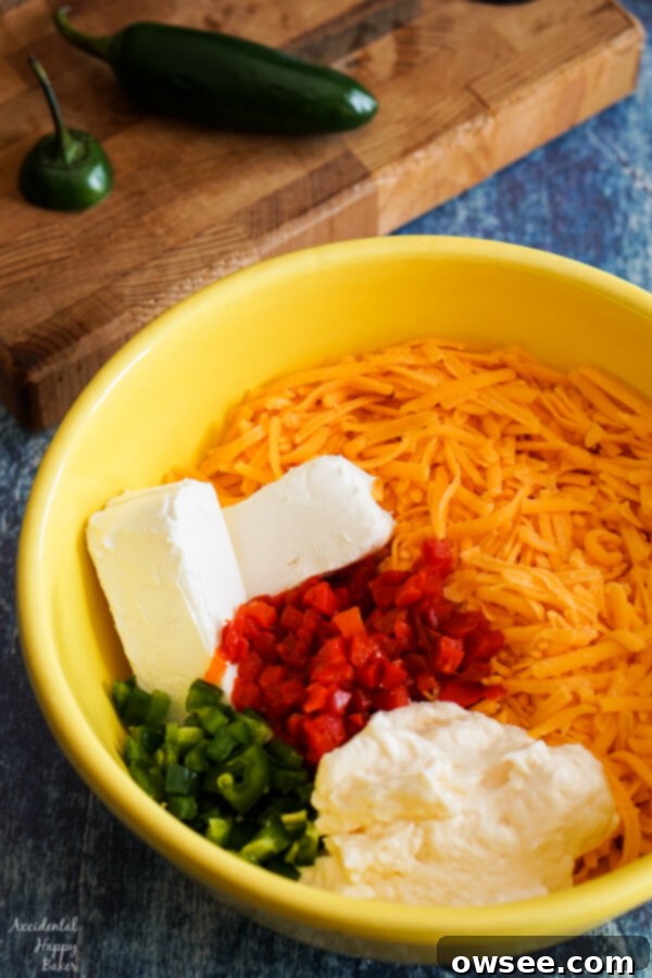 A bowl containing sharp cheddar cheese, cream cheese, mayonnaise, pimentos, and finely chopped jalapenos, ready to be mixed for pimento cheese.