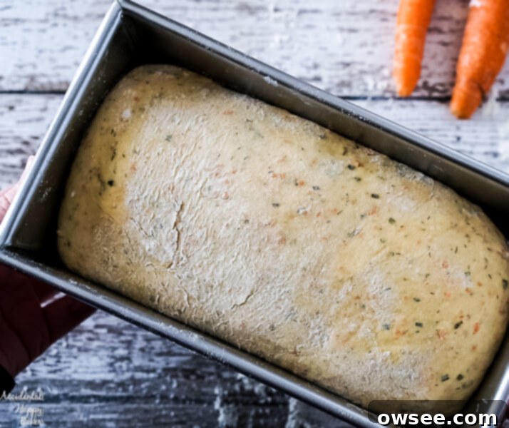 Carrot and chive bread dough shaped into a loaf and placed in a bread pan for its final rise.