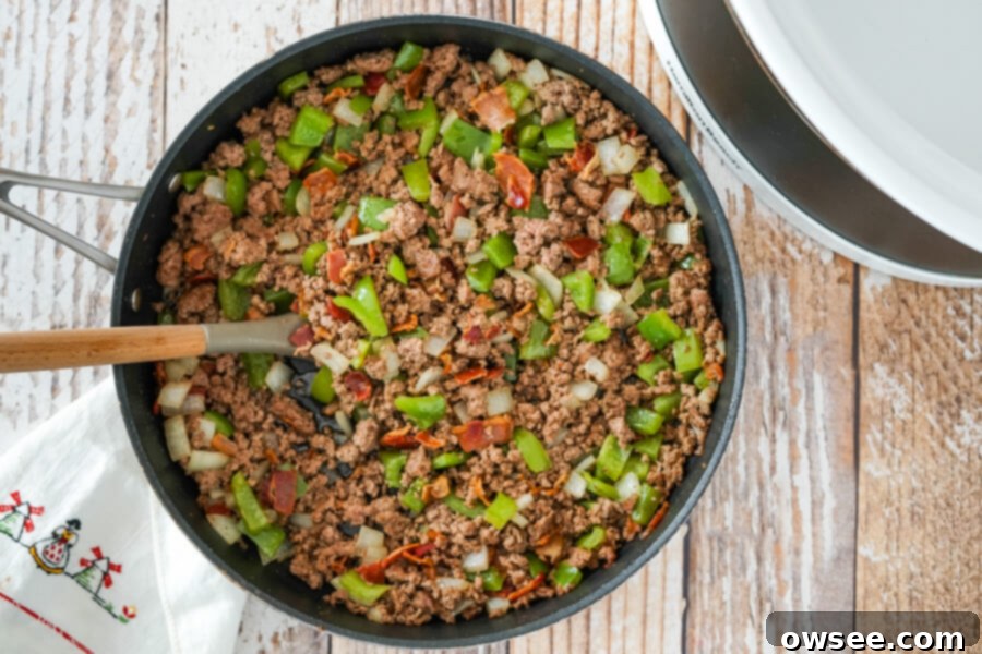 Ground beef, diced onions, and green peppers cooking in a skillet, browning for the Calico Beans recipe.