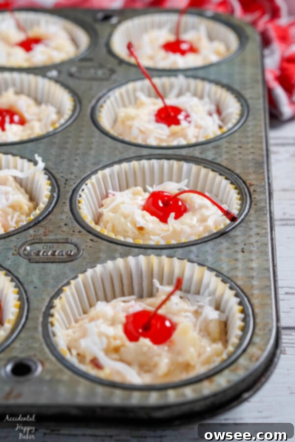 Malibu Dream Muffins 4 Maraschino cherries and shredded coconut are carefully pressed into the tops of unbaked muffins in a tin, preparing them for a beautiful, colorful finish.
