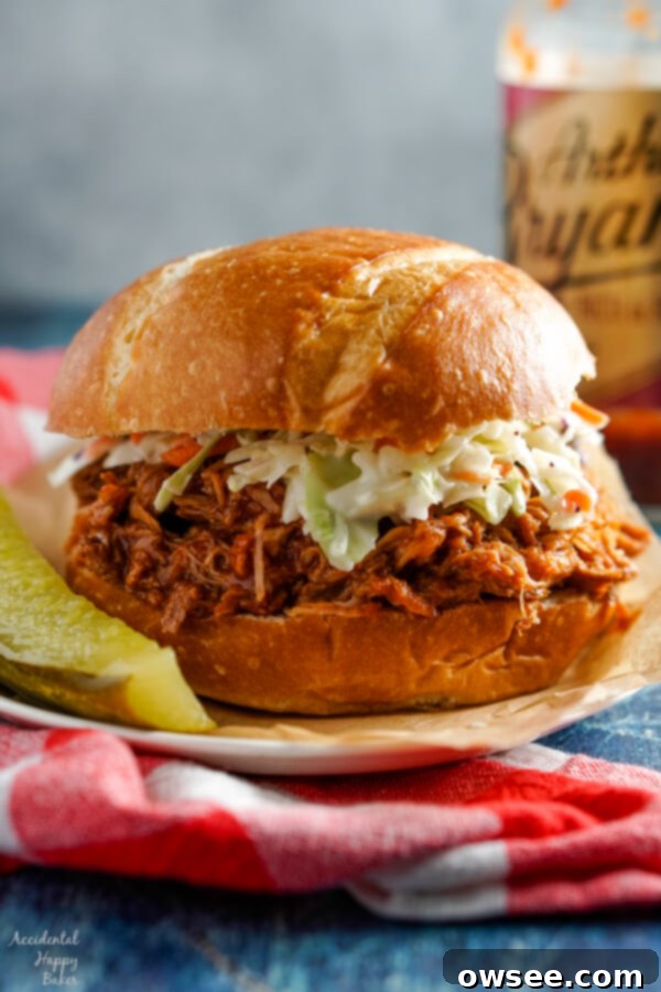Caramelized Root Beer Pulled Pork 2 A root beer pulled pork sandwich topped with creamy coleslaw, served alongside a dill pickle spear.