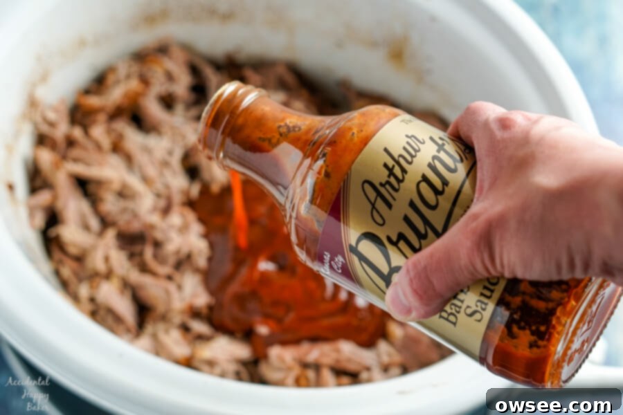 Caramelized Root Beer Pulled Pork 8 A bottle of rich barbecue sauce is poured generously over the shredded root beer pulled pork in the slow cooker, ready to be mixed for ultimate flavor.
