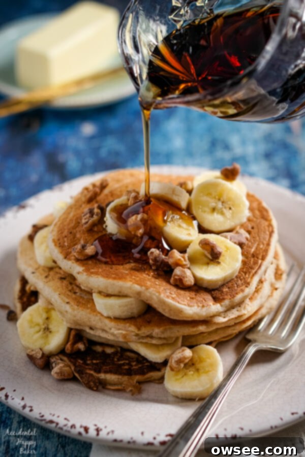 Maple syrup is poured over a stack of banana pancakes.