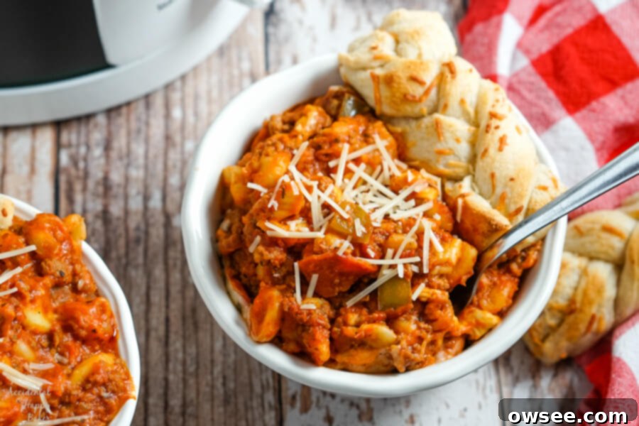 A bowl Crockpot Pizza Casserole with parmesan sprinkled on the top and a breadstick to the side. 