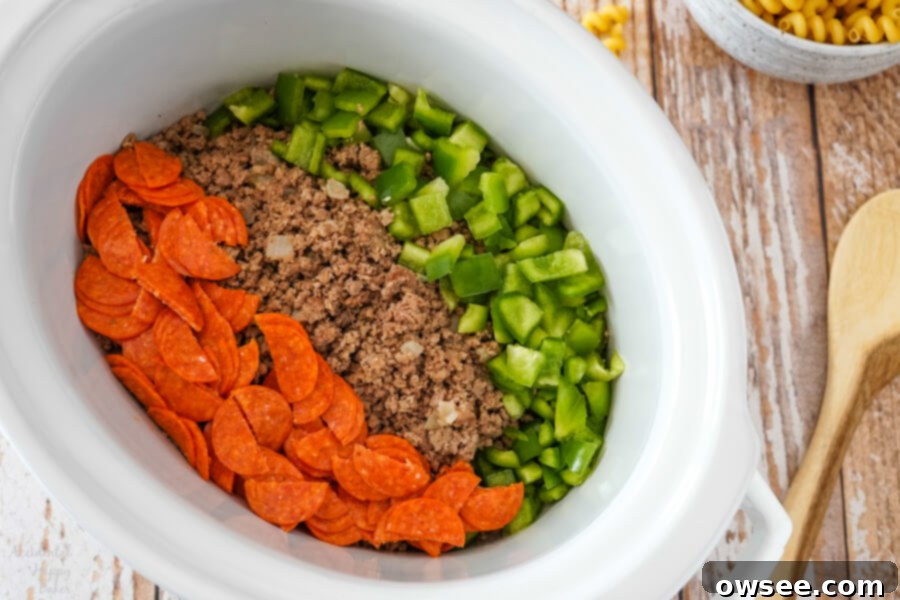 Browned hamburger and sausage are added to the slow cooker with vegetables. 