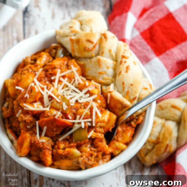 One-Pot Pizza Delight 8 A bowl of Crockpot Pizza Casserole with parmesan sprinkled on the top and a breadstick to the side.