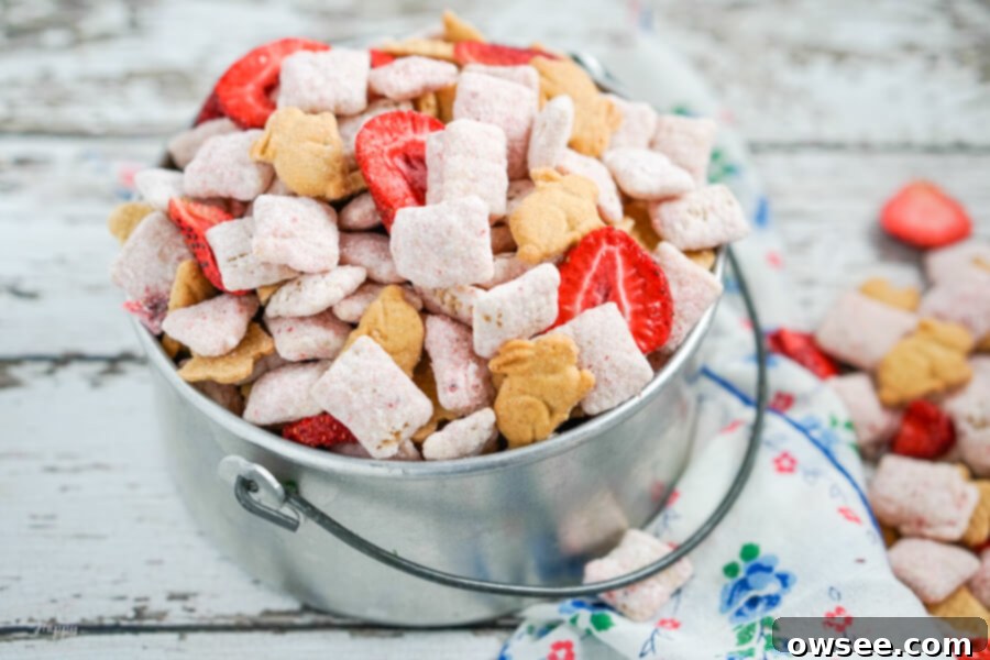 A silver bucket full of strawberry cheesecake muddy buddies with a blue flowered napkin beside it.