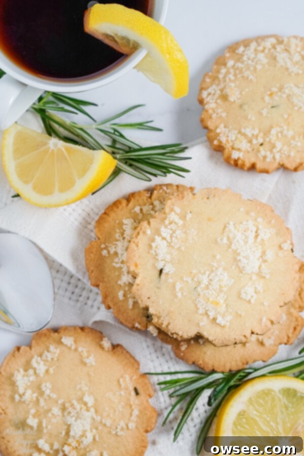Zesty Lemon Rosemary Cookies 8 Lemon Rosemary cookies, lemon slices and rosemary sprigs are spread on a white cloth napkin beside a cup of tea.