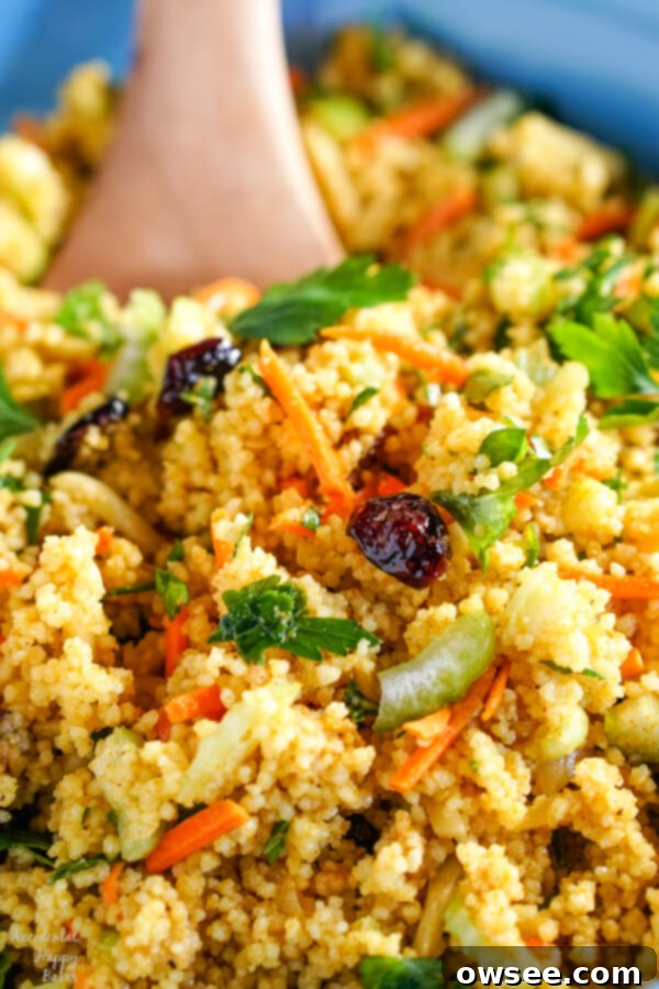 Sunshine Couscous Salad 2 A closeup shot of curried couscous salad in a blue bowl with a wooden spoon. The salad is vibrant with various colorful ingredients.