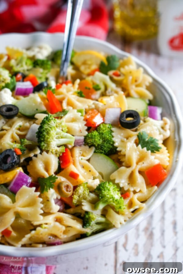 Bright Summer Pasta Delight 3 A vertical photo of a white bowl with summer vegetable pasta salad with a serving spoon.