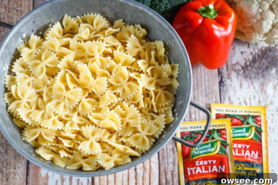 Bright Summer Pasta Delight 4 A colander of cooked pasta next to a pile of veggies and 2 packets of Italian dressing mix.