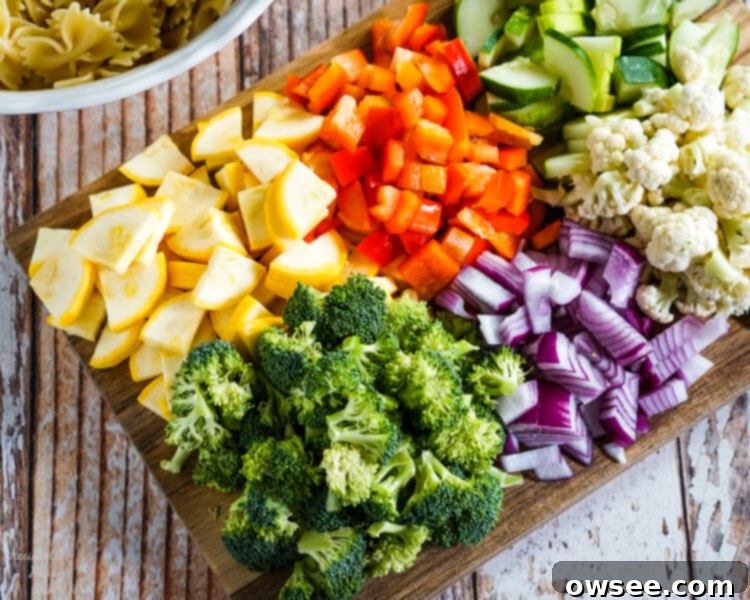 Bright Summer Pasta Delight 5 A wooden cutting board loaded with chopped yellow squash, red bell pepper, cucumber, broccoli, red onion, and cauliflower.