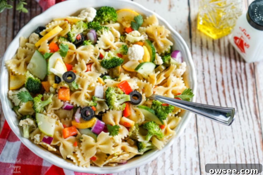 Bright Summer Pasta Delight 6 Summer vegetables and farfelle pasta tossed with an Italian dressing in a white bowl. A bottle of olive oil and pepper sit to the side.