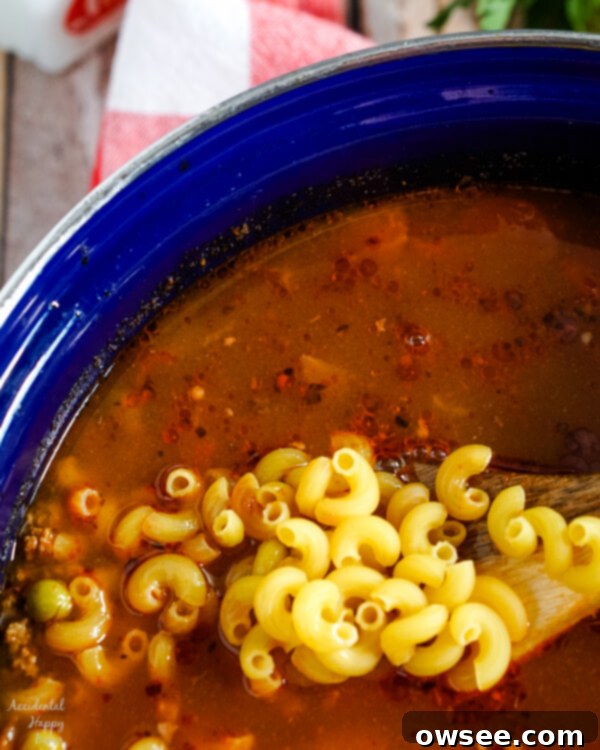 A large pot of Hamburger Macaroni Soup simmering on the stove, with elbow macaroni just added, promising a hearty meal.
