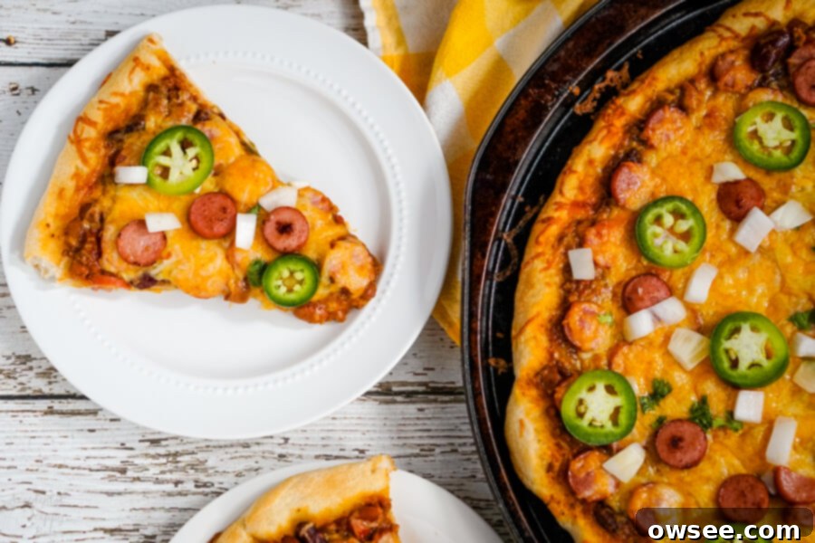 A delicious slice of Chili Dog Pizza topped with chili, hot dogs, and melted cheese on a white plate, ready to be enjoyed.