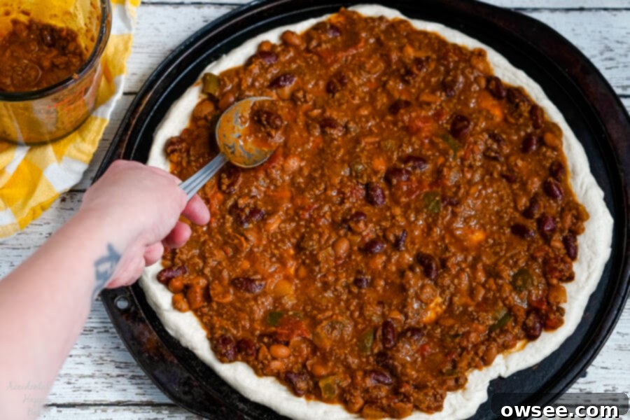Chili Dog Pizza Fusion 4 Smooth, rich chili is generously spread as the sauce over the raw pizza dough, forming the base for Chili Dog Pizza.