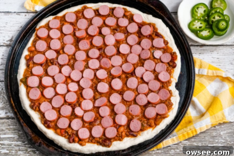 Chili Dog Pizza Fusion 5 Thinly sliced hot dog pieces are arranged neatly over the chili base on the pizza dough, ready for cheese.