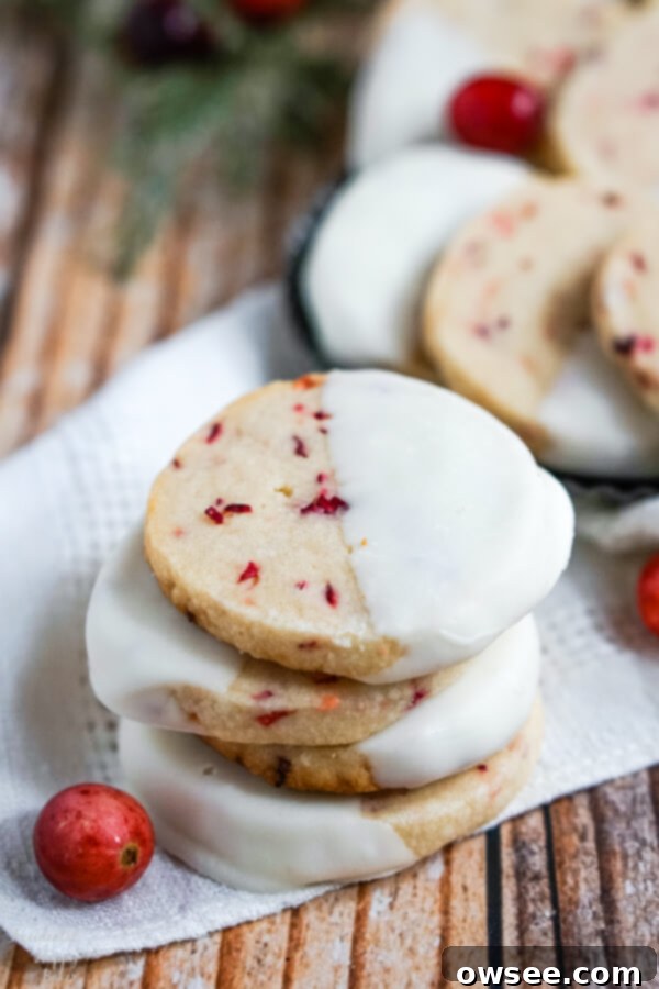 Buttery White Chocolate Cranberry Shortbread Cookies 9 A stack of White Chocolate Cranberry Shortbread Cookies sitting on a white napkin with a cranberry to one side.