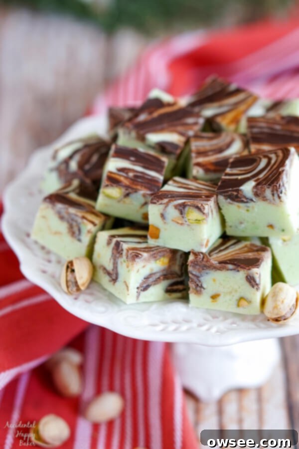 A white platter stacked high with Pistachio Swirl Fudge and pistachios, showcasing its creamy texture and dark chocolate swirls.