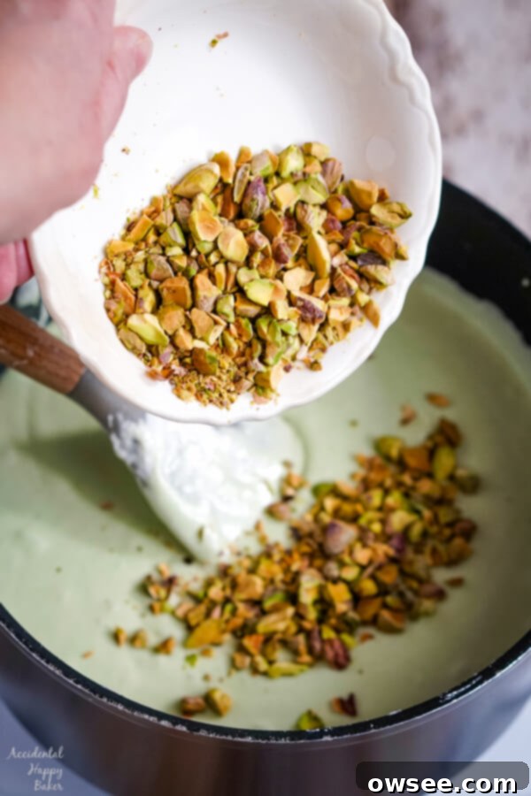 Chopped pistachios are being stirred into the smooth and creamy pistachio fudge base in a saucepan.