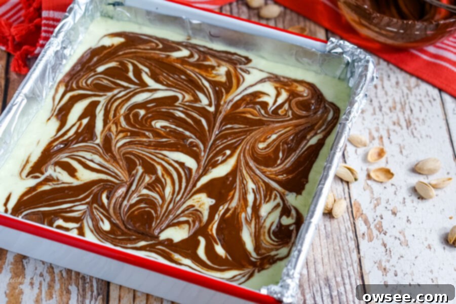 After the dark chocolate is swirled into the pastel green pistachio fudge, the pan is covered and placed in the fridge to set completely.